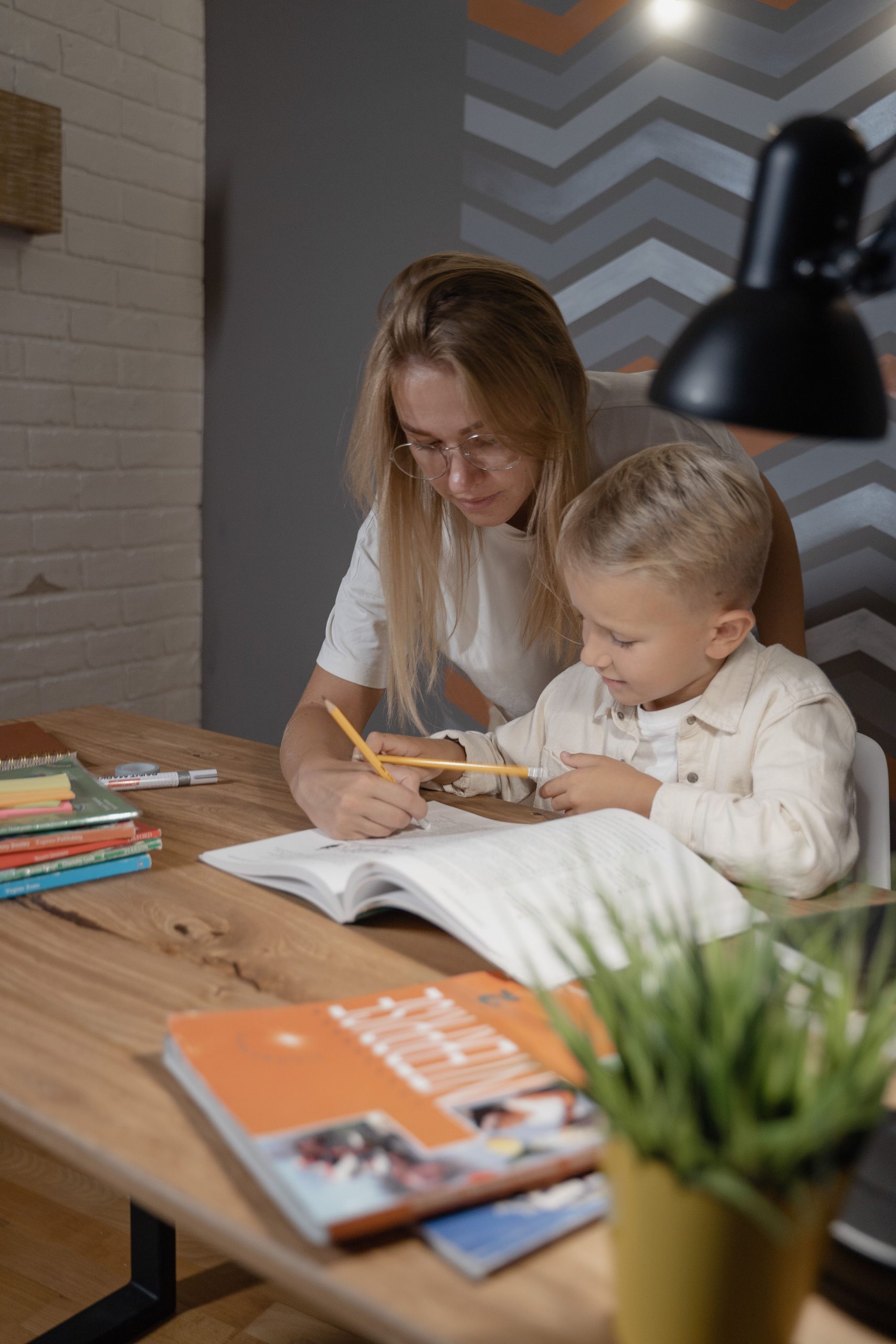 Mother guiding young child in homework indoors, promoting learning and education.