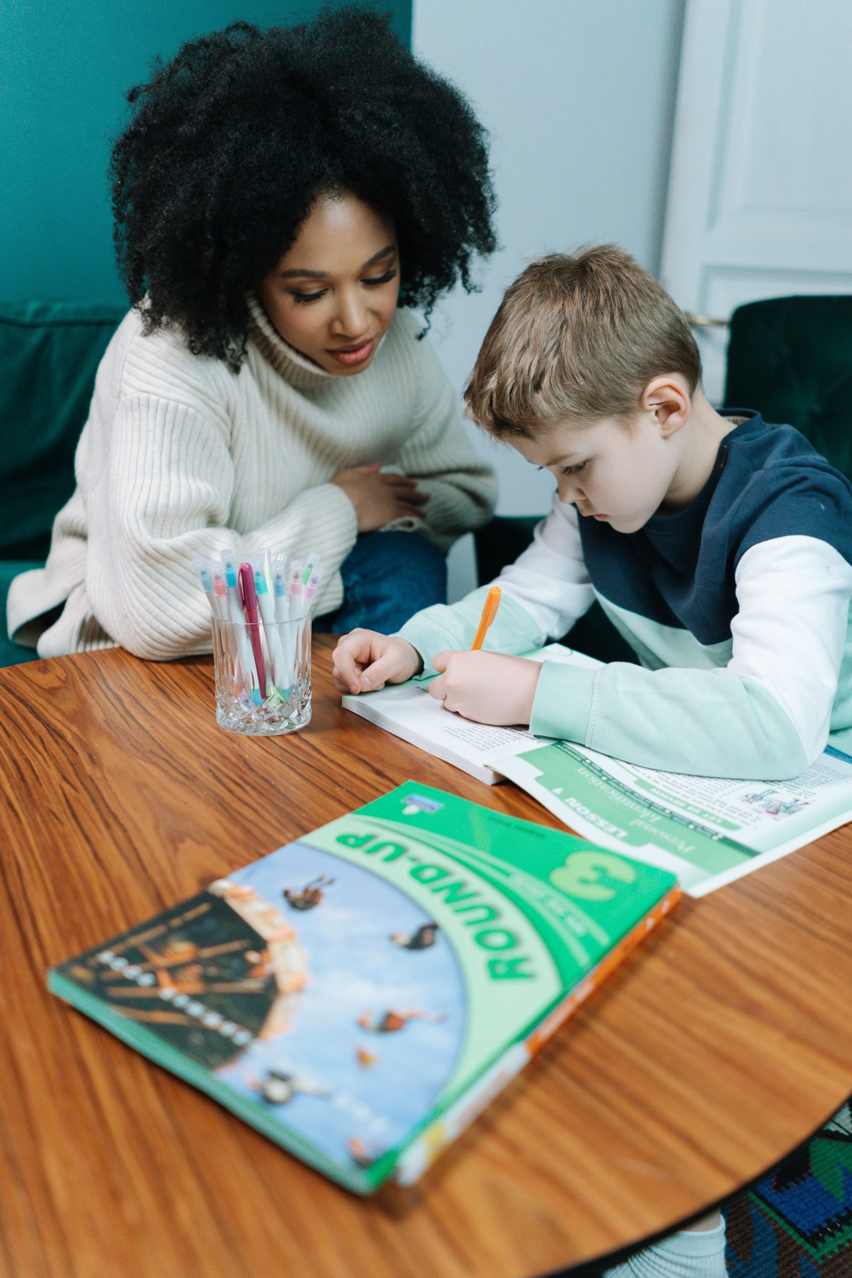 A woman helps her son with his homework at a table, fostering learning and understanding.