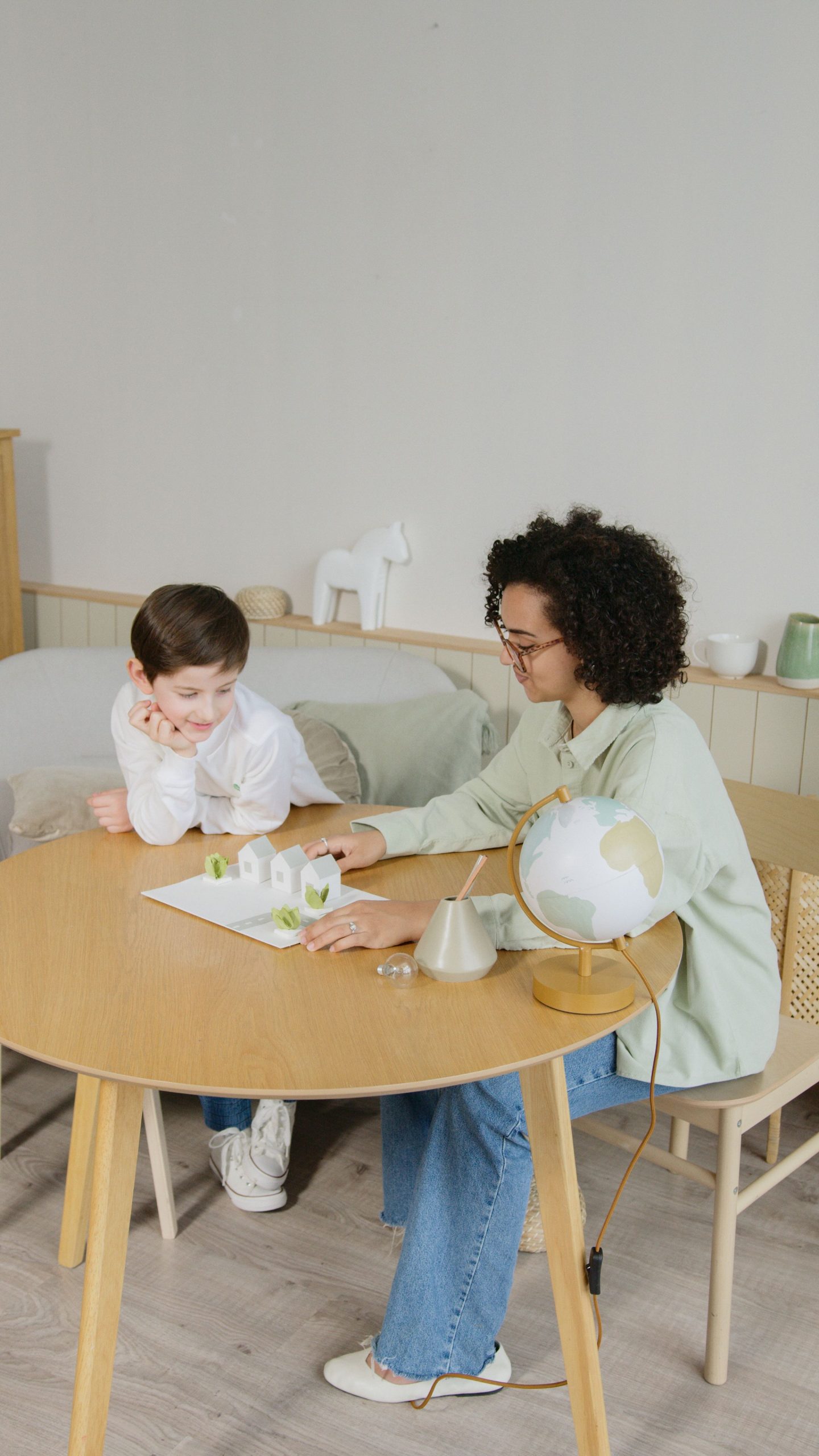A child learns geography in a home setting with a teacher, emphasizing interactive education.